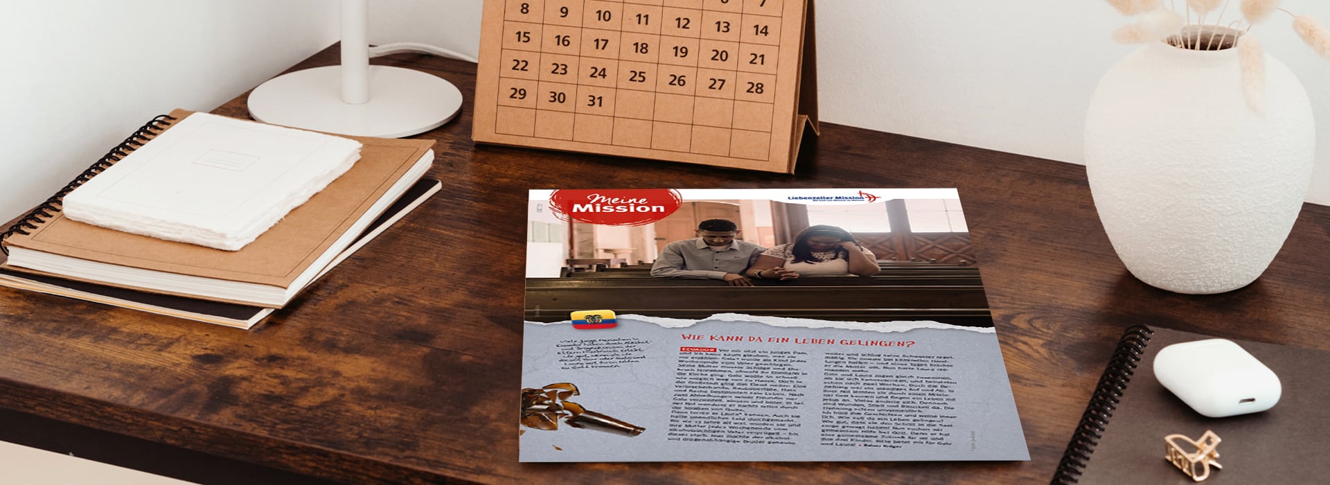 Ein Schreibtisch, auf dem ein Notizbuch, ein Kalender, eine Vase und eine Seite aus einer deutschen Zeitschrift mit dem Titel „Meine Mission“ liegen.