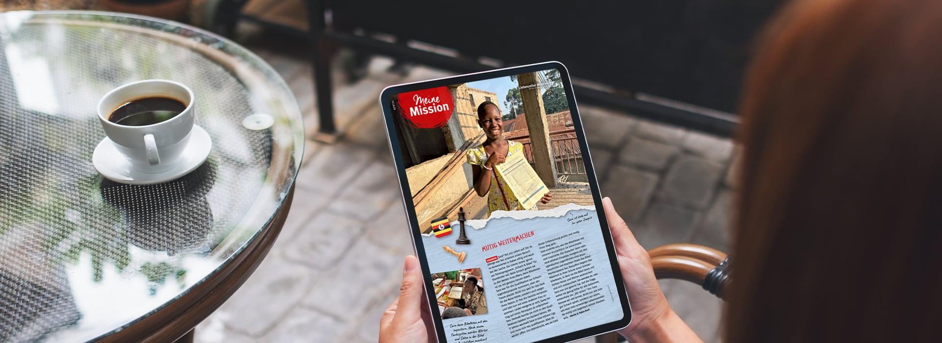 Eine Person, die an einem Tisch im Freien einen Artikel auf einem Tablet liest, daneben steht eine Tasse Kaffee.