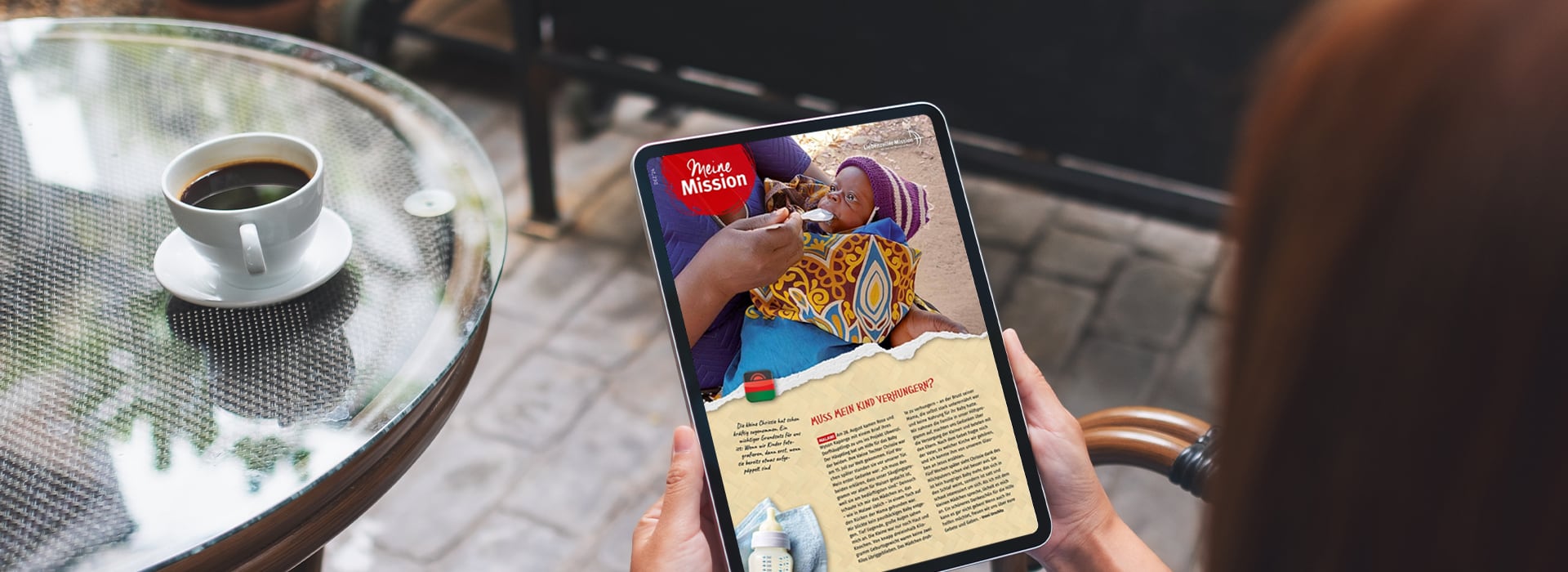 Eine Person liest auf einem Tablet ein digitales Magazin an einem Tisch im Straßencafé, neben ihr steht eine Tasse Kaffee.