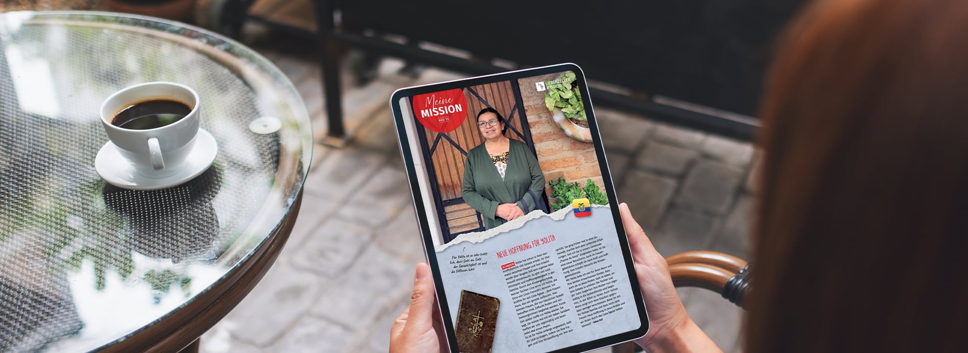 Eine Person liest an einem Tisch im Freien bei einer Tasse Kaffee ein digitales Magazin auf einem Tablet.
