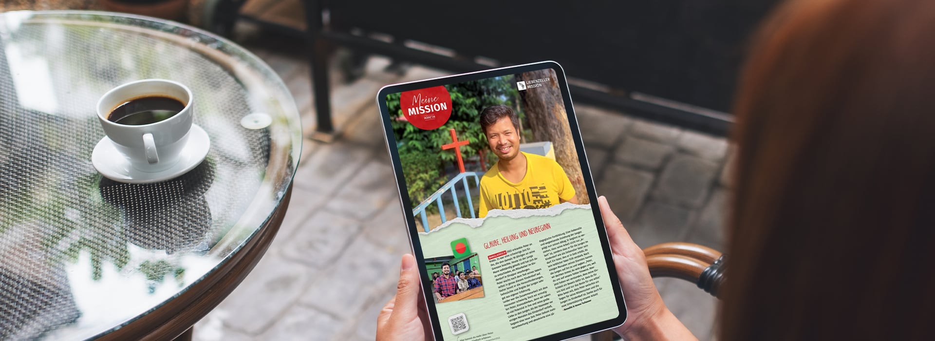 Eine Person, die ein Tablet in der Hand hält, auf dem ein Zeitschriftenartikel zu sehen ist; daneben steht eine Kaffeetasse auf einem Glastisch.