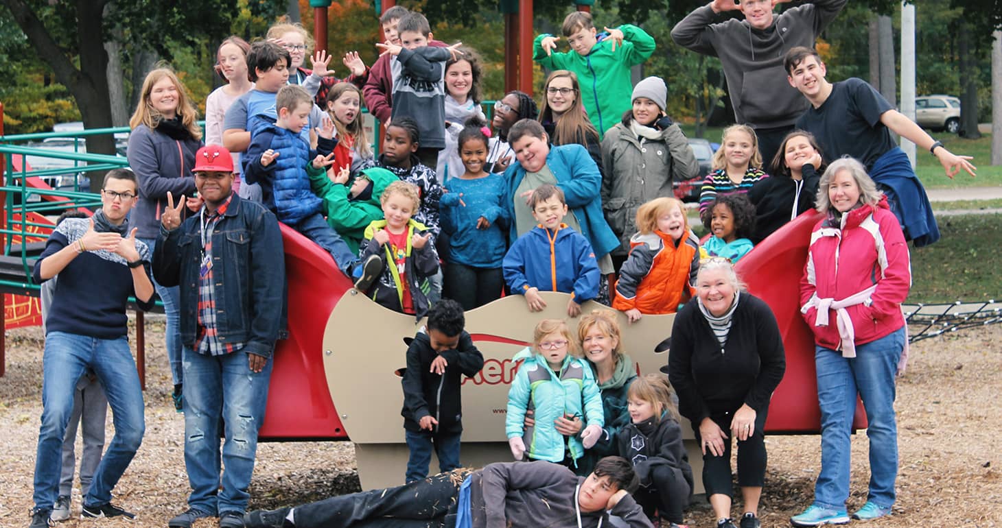 Eine große Gruppe von Kindern und Erwachsenen posiert spielerisch auf den Spielgeräten im Freien in einem Park.