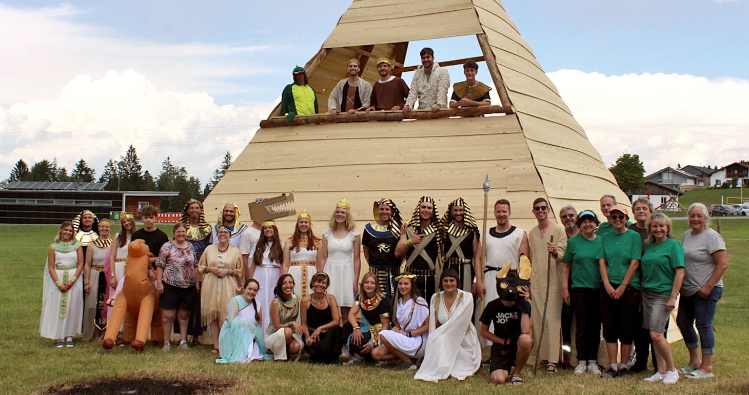 Eine Gruppe in ägyptischen Trachten posiert an einem sonnigen Tag im Freien vor einer großen Holzpyramide.