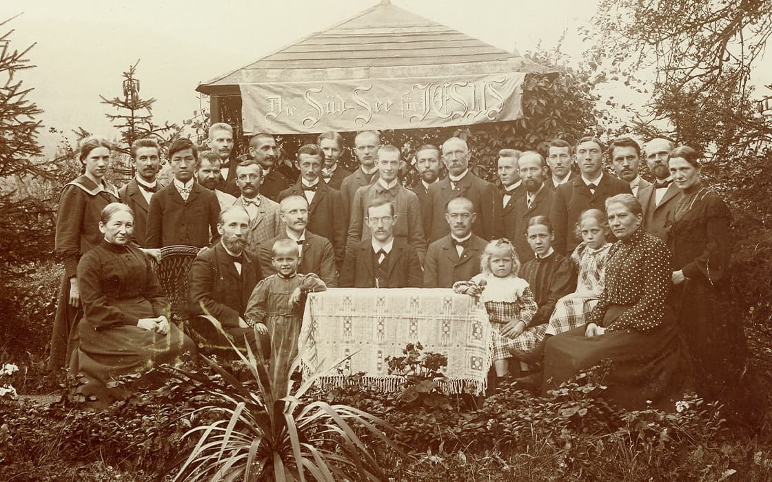 Eine große Gruppe von Männern, Frauen und Kindern posiert vor einem Banner für ein formelles Porträt im Freien.