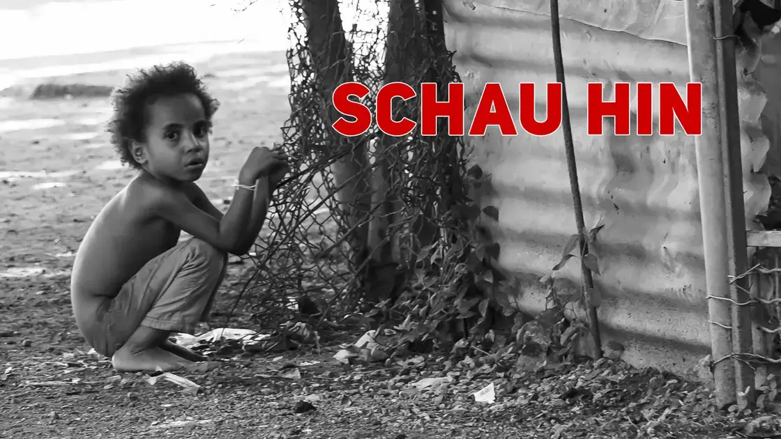 Ein kleines Kind hockt an einem Zaun neben einer Wellblechwand; in kräftigem Rot steht dort „SCHAU HIN“.