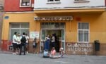 Vor einem gelben Gebäude mit der Aufschrift „Misión Evangélica Urbana“ stehen und sitzen Menschen. Kinder sitzen auf dem Bürgersteig.