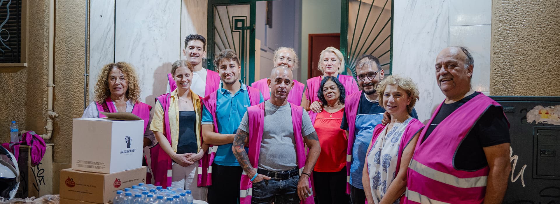 Eine Gruppe von zehn Personen, von denen einige rosa Warnwesten tragen, posiert vor einem Gebäude für ein Foto.