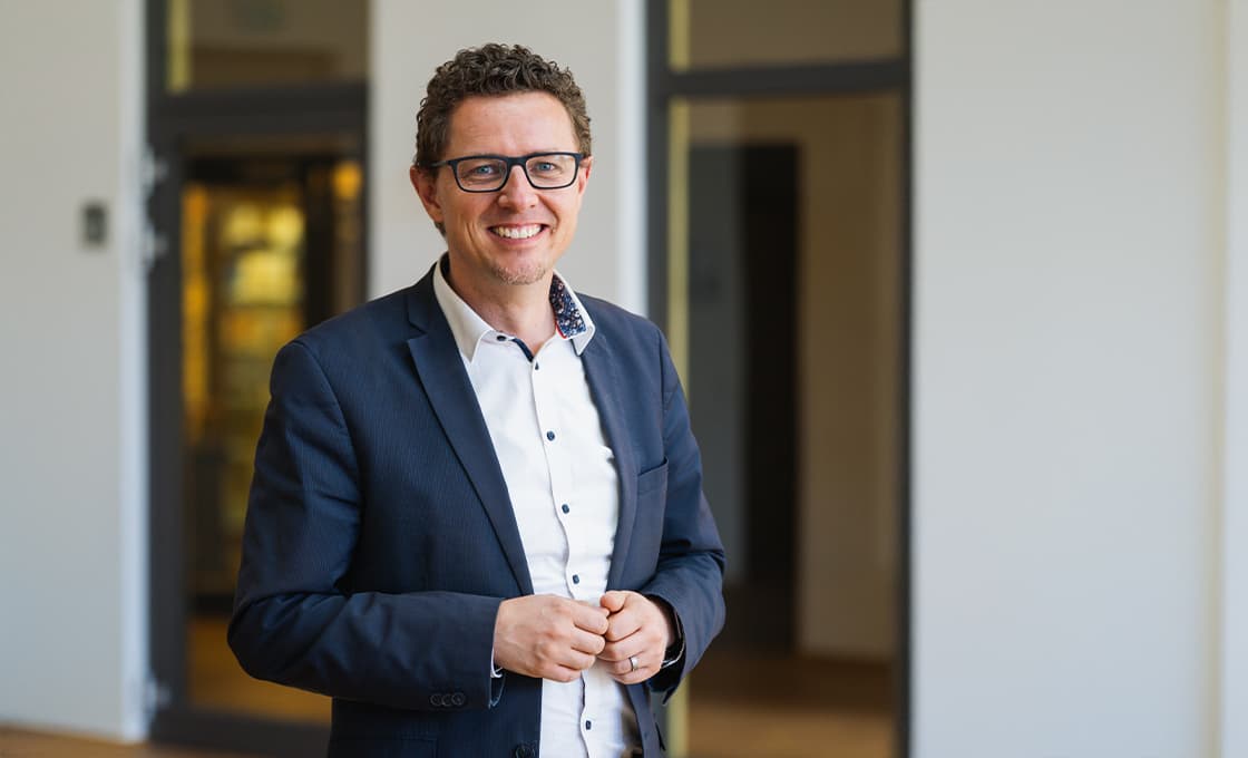 Ein lächelnder Mann in Blazer und Hemd, der in einem Büroflur steht.