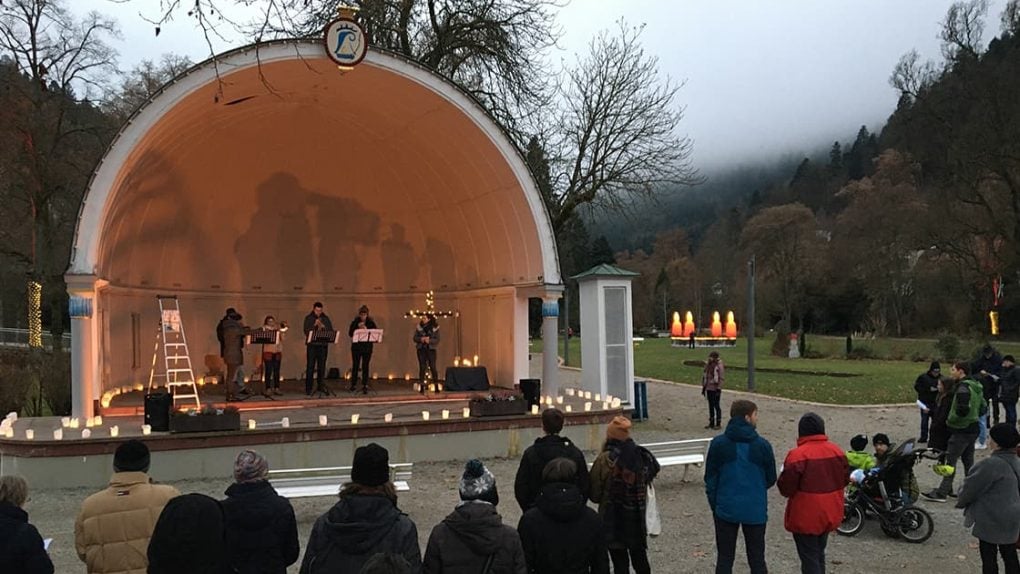 Auf einer beleuchteten Freilichtbühne, umgeben von Bäumen, feiern die Menschen den Advent 2025 im Park mit Musikern.
