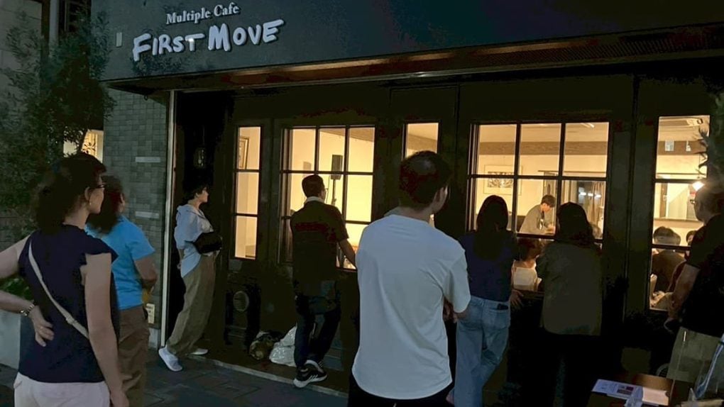 Menschen in Japan stehen vor dem FIRST MOVE Cafe und blicken auf eine lebhafte evangelistische Trickshow-Veranstaltung bei Nacht.