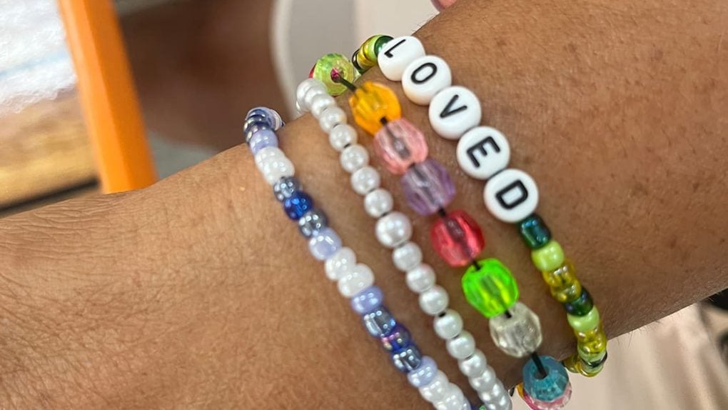 Vier bunte Perlenarmbänder an einem Handgelenk, eines mit weißen Perlen mit der Aufschrift "LOVED".