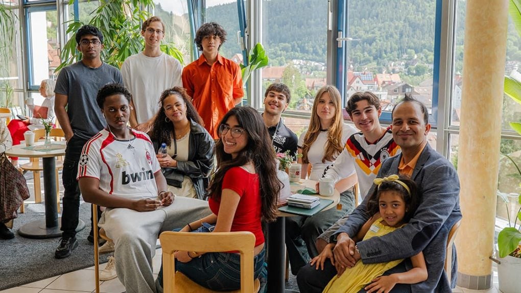 Eine bunte Gruppe von Menschen, Erwachsene und Kinder, sitzt und steht lächelnd in einem hellen Café mit großen Fenstern.
