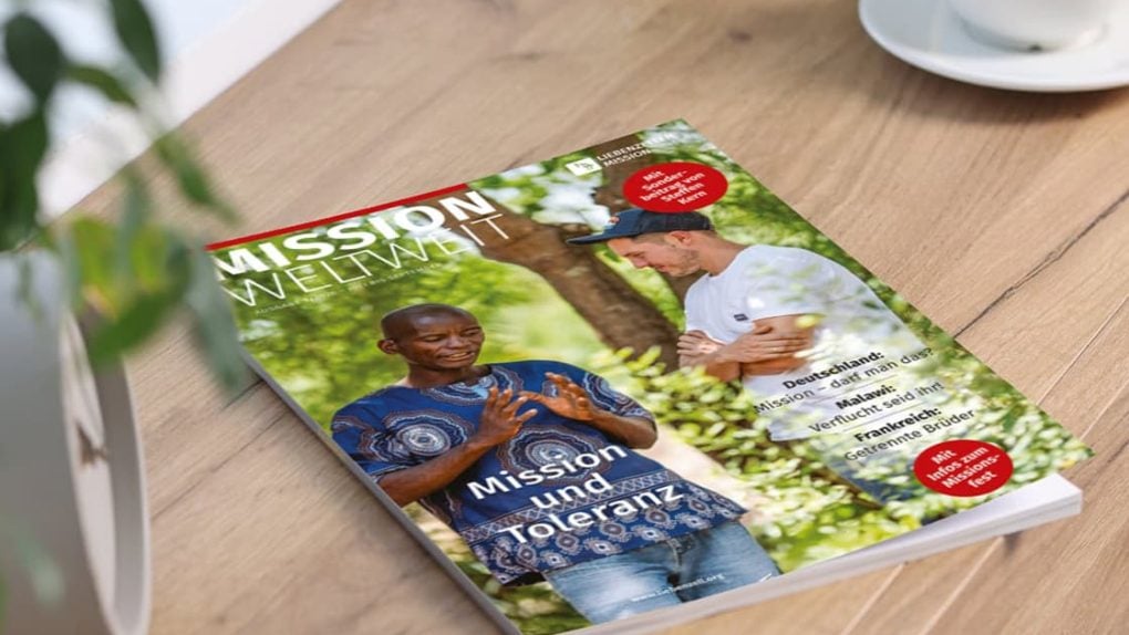 Die Zeitschrift „Mission Weltweit“ liegt auf einem Tisch; darauf sind zwei Männer zu sehen, die sich im Freien unterhalten, einer davon in traditioneller Tracht.