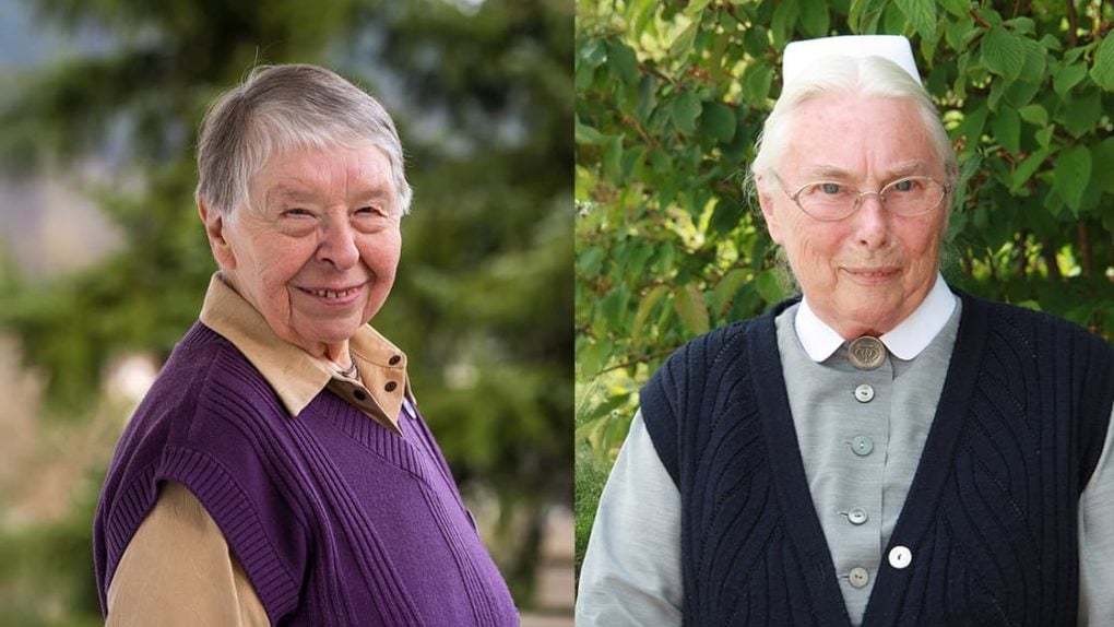 Zwei ältere Frauen, die beide im Freien lächeln; die eine trägt eine lila Weste, die andere eine marineblaue Weste und eine weiße Mütze.