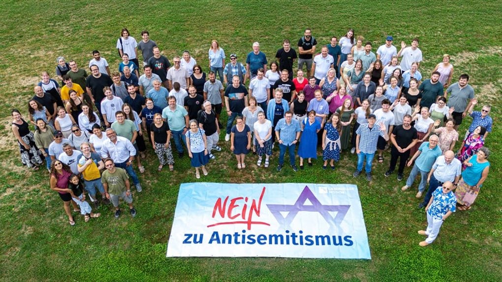 Eine große Gruppe steht auf einer Wiese hinter einem Transparent mit der Aufschrift „Nein zu Antisemitismus“ und einem durchgestrichenen Davidstern.