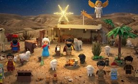 LEGO-Krippe bei Nacht mit Figuren, Tieren, einem Engel und einem Stern über einem Stall in einer Wüstenlandschaft.