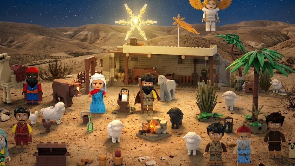 LEGO-Krippe bei Nacht mit Figuren, Tieren, einem Engel und einem Stern über einem Stall in einer Wüstenlandschaft.