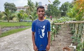 Ein lächelnder Junge in einem blauen T-Shirt steht auf einem Weg in einem Garten.