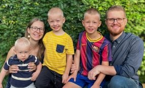 Eine vierköpfige Familie, die draußen vor einer Hecke für ein Foto posiert.