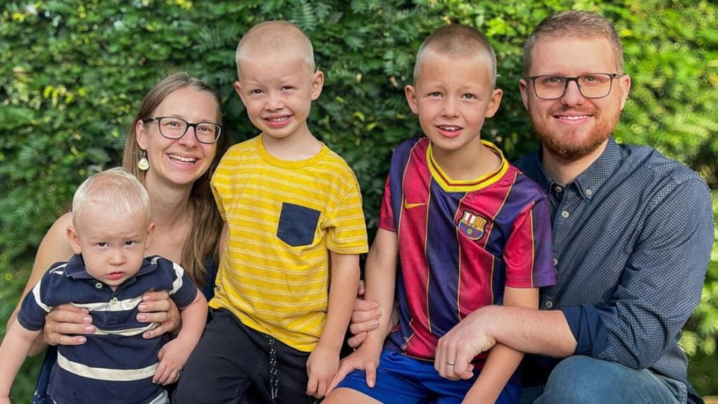 Eine vierköpfige Familie, die draußen vor einer Hecke für ein Foto posiert.