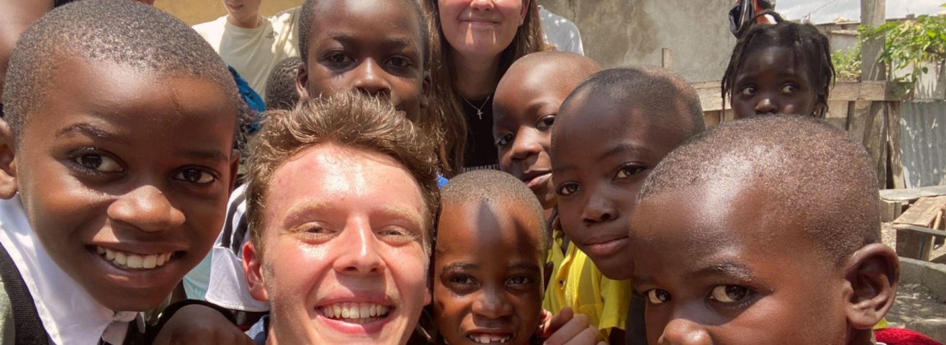 Eine Gruppe lächelnder Kinder und zwei Erwachsene posieren an einem sonnigen Tag im Freien dicht beieinander für ein Selfie.